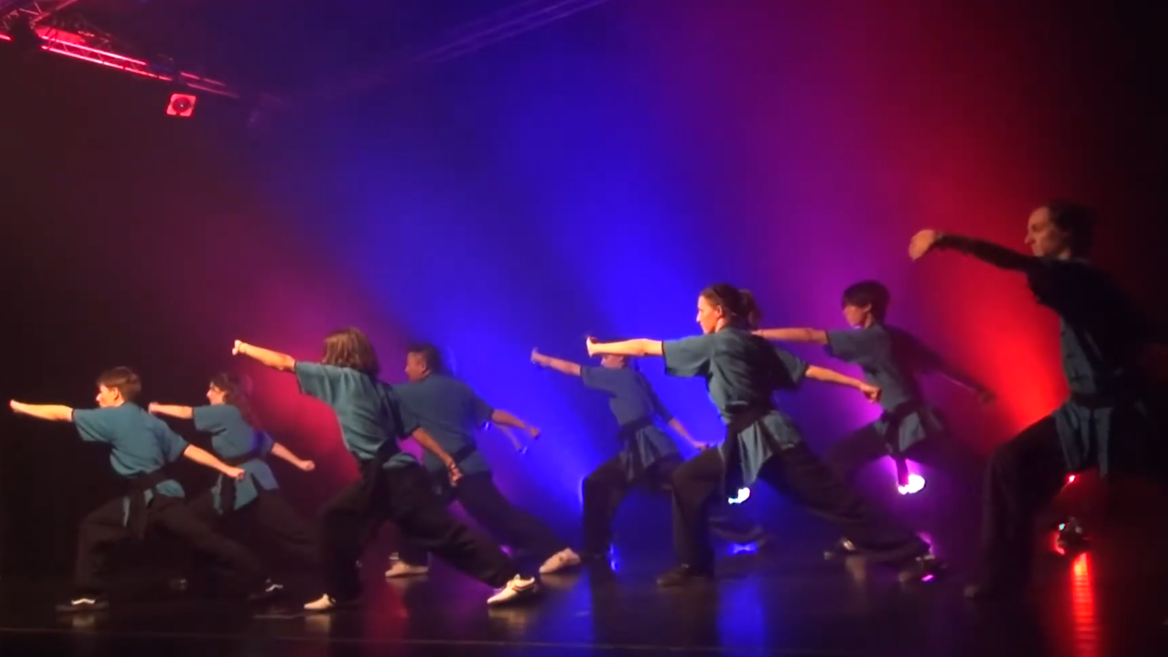 Un groupe de personne effectue un mouvement synchronisé de kung fu sur une scène